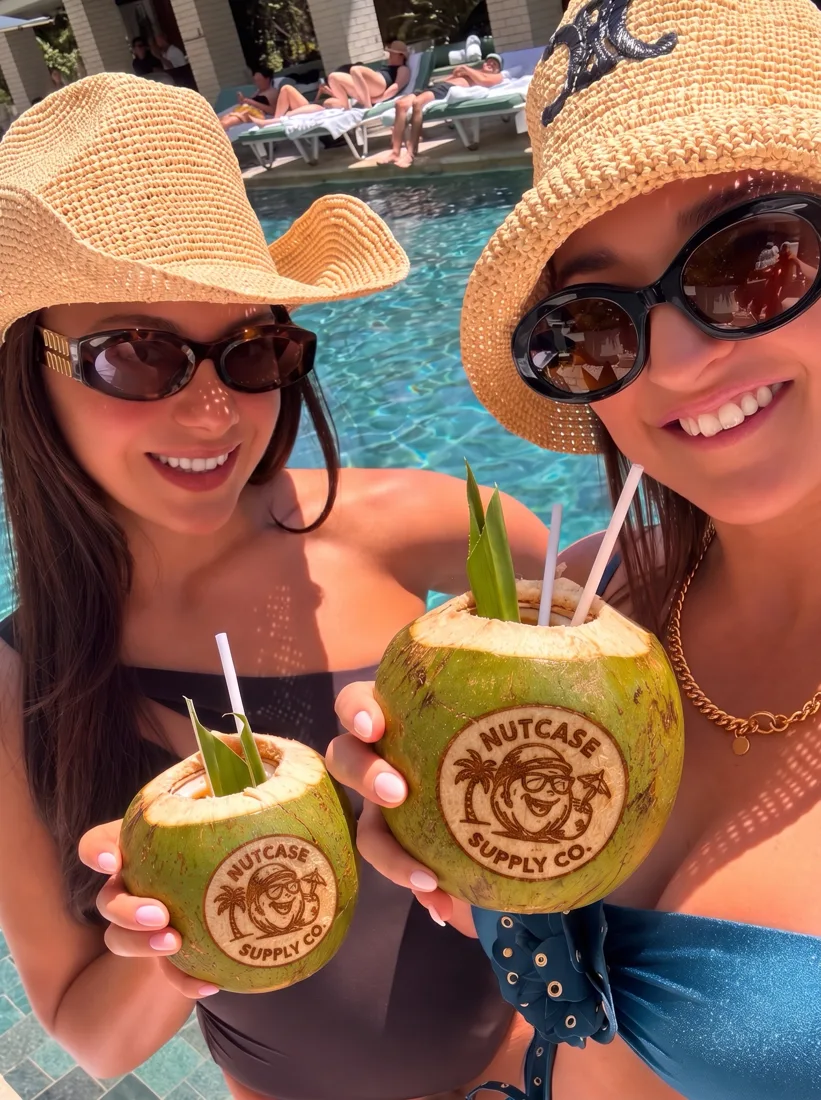 Two friends at a resort pool holding Nutcase coconuts